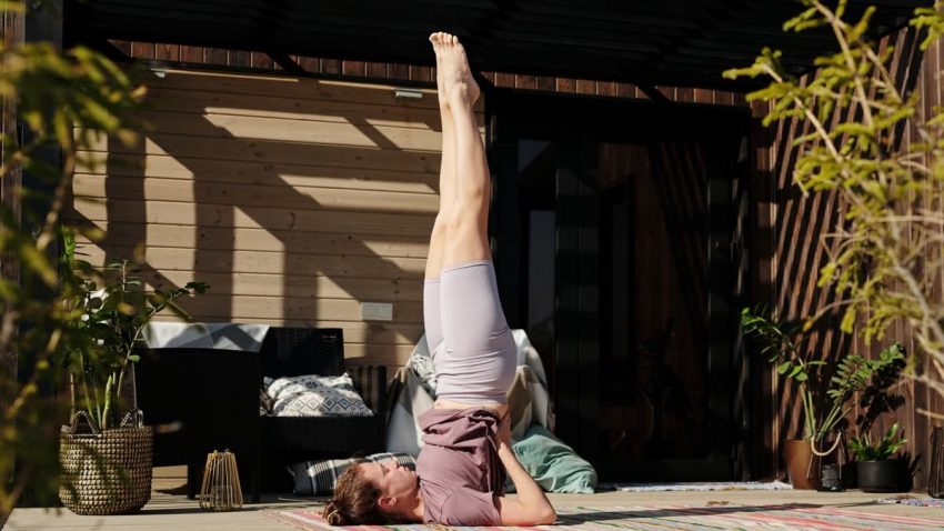 A woman performing a shoulder stand yoga pose on a sunny outdoor patio, enhancing flexibility and mindfulness.